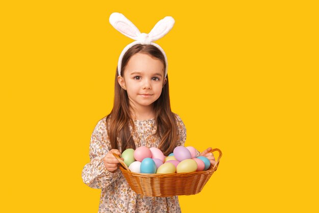 Close up portrait of a little girl holding a basket of colourful eggs Studio shot over yellow background