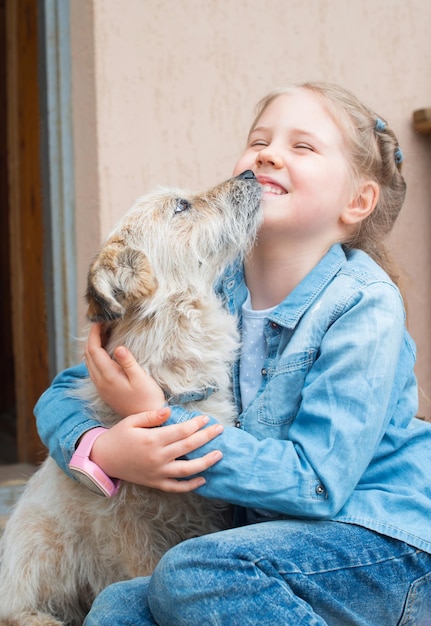 Close up portrait of little girl hugging her dog friend outdoors and laughing