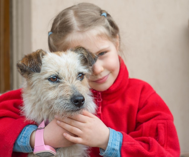 Close up portrait of little girl hugging her mongrel dog friend outdoors and smiling