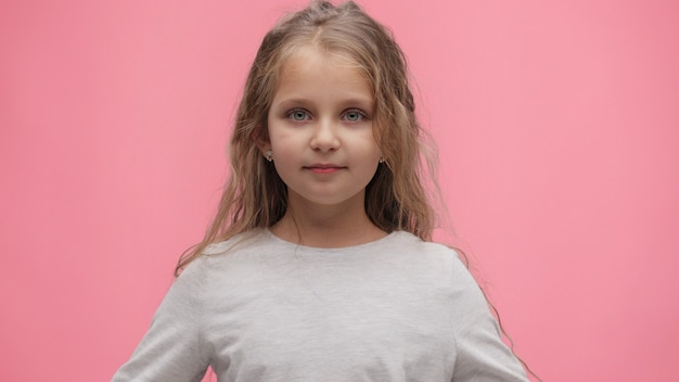 Close up portrait of little girl at pink background. Cute curly-haired girl looking at camera.