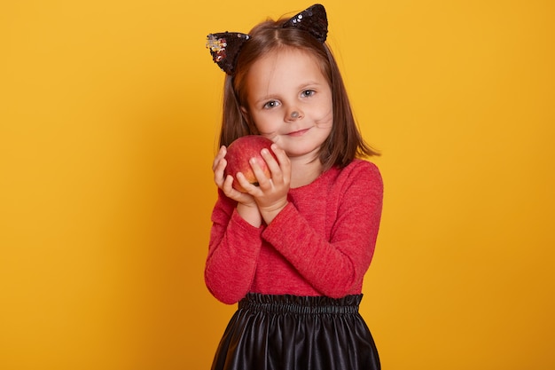 Close up portrait of little girl wearing cat's costume holding red poisoned apple