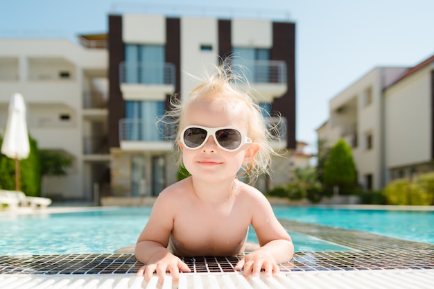 Close-up portrait of little girl with sunglasses in pool on vacation.