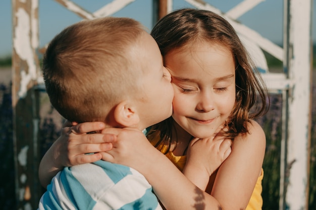 Foto chiuda sul ritratto di un ragazzino adorabile che abbraccia e bacia la sorella all'aperto al tramonto.