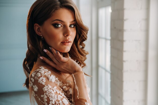 Close-up portrait of a luxurious bride in a wedding dress in the morning in her interior.