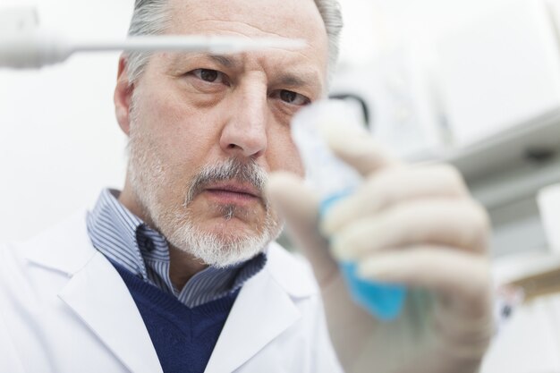 Close-up portrait of a male researcher holding flask with blue liquid in the lab