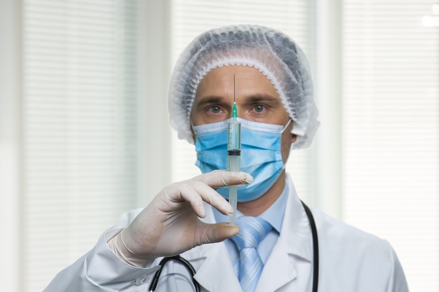 Photo close up portrait of male surgeon holding syringe. caucasian mature physician is standing in a room.