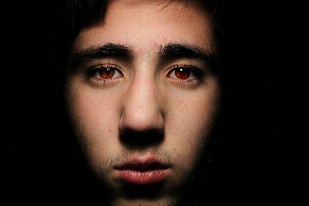 Photo close-up portrait of man with red eyes against black background