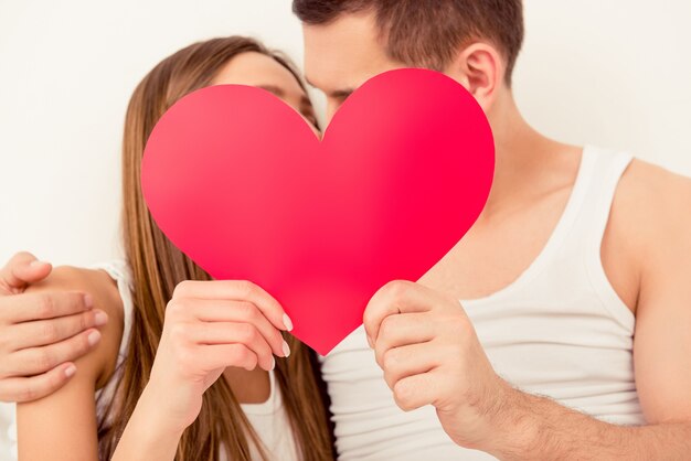 Close up portrait of man and woman kissing behind paper heart