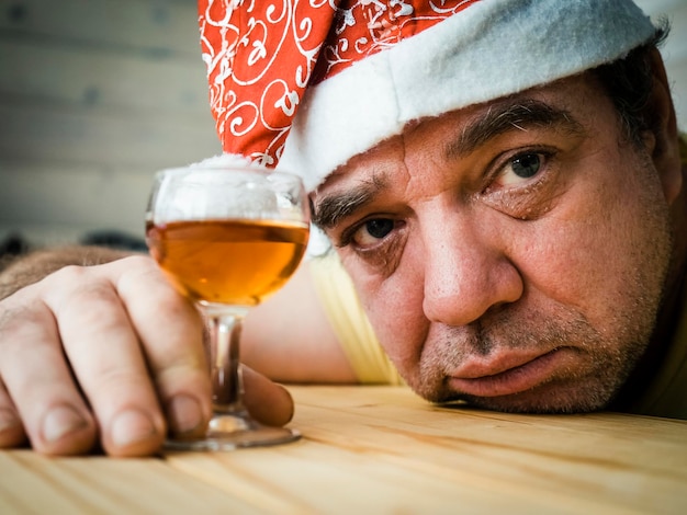 Photo close-up portrait of mature man wearing santa hat holding drink on table