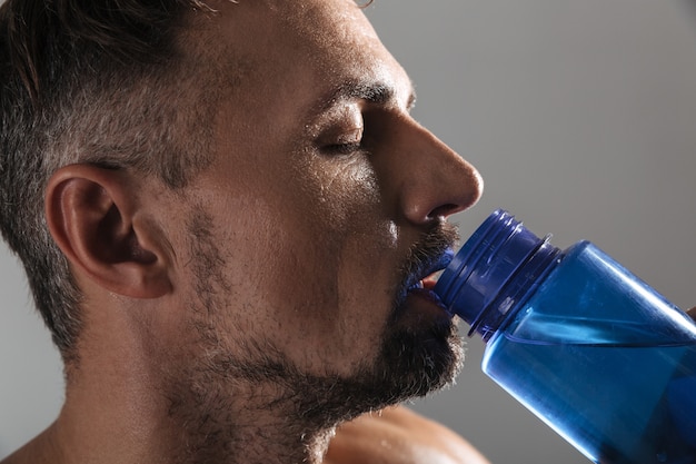 Close up portrait of a mature shirtless sportsman drinking water