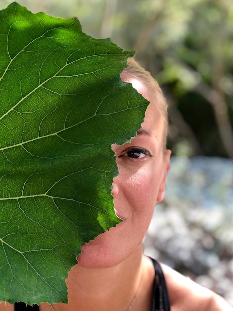 Close-up portrait of mid adult woman hiding behind leaf