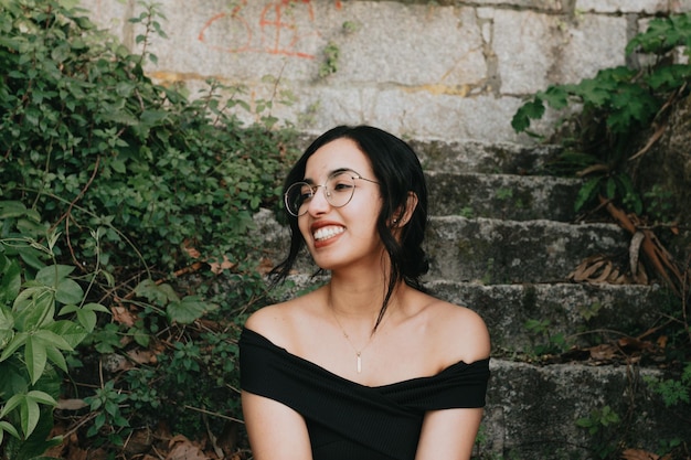 Close up portrait of a modern young woman sitting on stairs smiling away from camera Mental health and happiness concept Free time on young people and leisure time Travel on vacation