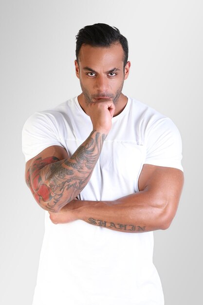 Photo close-up portrait of a muscular  tattooed guy wearing white shirt holds hand on chin