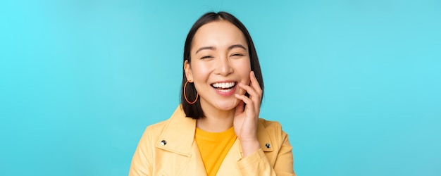 Close up portrait of natural asian girl laughing smiling and looking happy standing over blue background