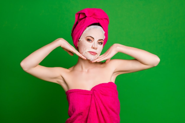 Close-up portrait of nice attractive healthy lady wearing turban collagen facial cotton mask touching isolated on bright green color background