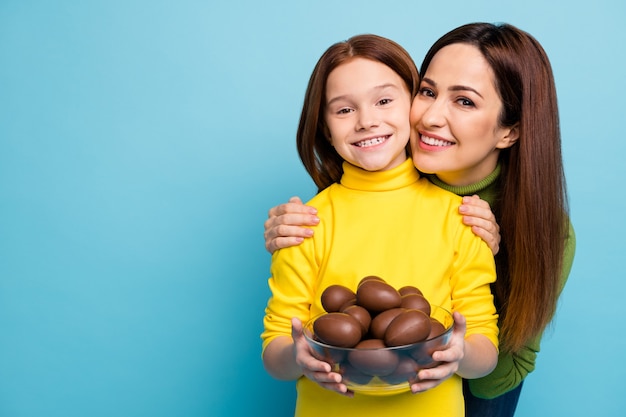 Close-up portrait of nice attractive lovely charming kind careful cheerful cheery girls holding in hands sweet eggs hugging isolated over bright vivid shine vibrant blue color