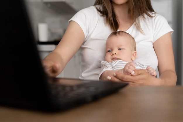Close up portrait of a nursing baby. The boy sits in his mother's arms. A woman works at home with a laptop.
