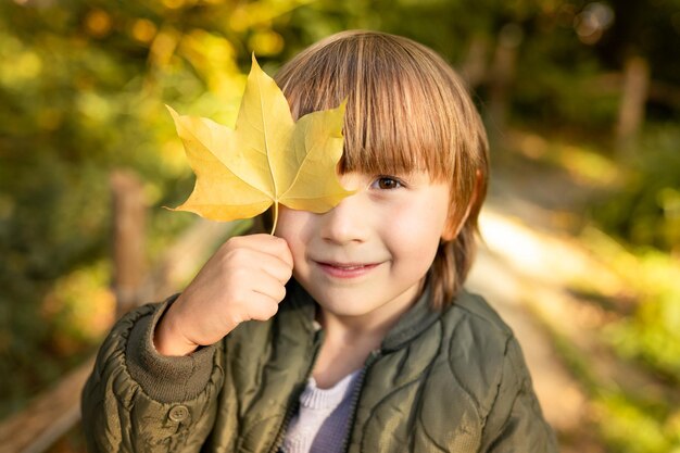 写真 公園で歩いている秋の幼児の男の子の手にメープル葉を持った男の子のクローズアップ肖像画