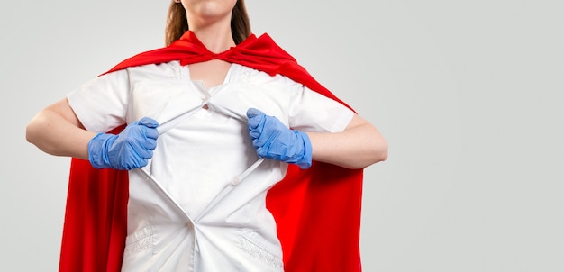 Крупным планом портрет женщины-врача в медицинских перчатках и красной накидке супергероя, разрывает пальто на груди. серый фон. скопируйте пространство. концепция силы супергероя для медицины.