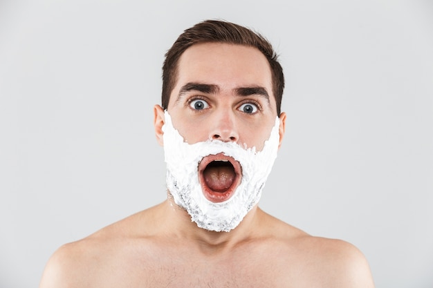 Крупным планом портрет красивого бородатого мужчины с пеной для бритья на лице, изолированном над белой