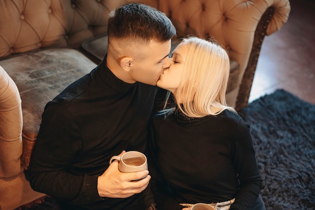 Фото Крупным планом портрет прекрасной молодой пары, целующейся на полу у себя дома, попивая горячий кофе на диване.