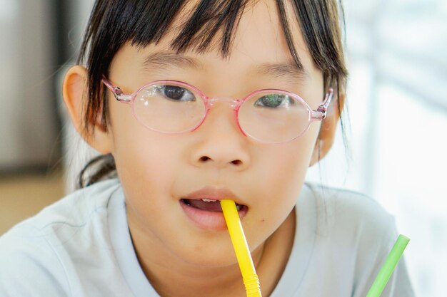 写真 ストローから水を飲んでいる眼鏡をかけた女の子のクローズアップ肖像画