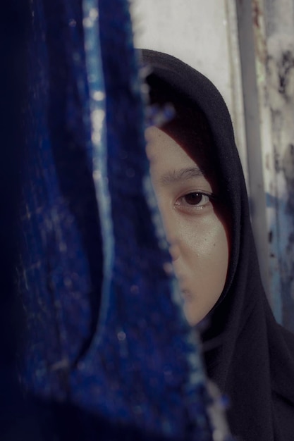 写真 カーテンに囲まれたヒジャブを着た若い女性のクローズアップ肖像画