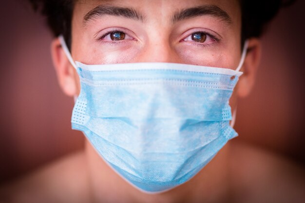 Close up and portrait of one millennial teenager man looking at the camera sad wearing mask ad crying for the covid-19