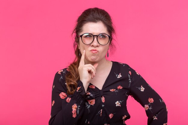 Close-up portrait of pensive serious young charming woman in glasses posing on a pink wall. Concept of dreams and ideas. promo space