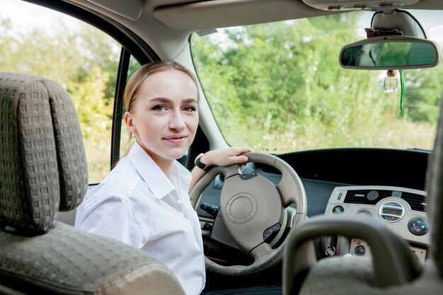 Close up portrait of pleasant looking female with glad positive expression being satisfied with unforgettable journey by car sits on driver s seat People driving transport concept