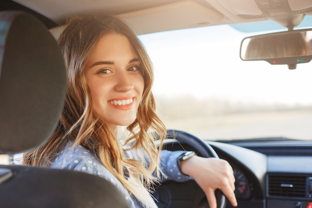 Photo close up portrait of pleasant looking female with glad positive expression, being satisfied with unforgettable journey by car, sits on driver seat, enjoys music.