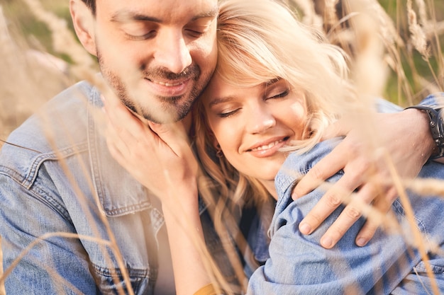 Close up portrait of a pleased man and his joyous girlfriend with their eyes closed sitting outdoors