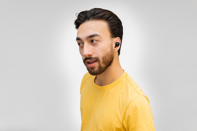 Close up portrait of a portrait of a young latin man in profile
surprised with wireless earphones looking away white
background