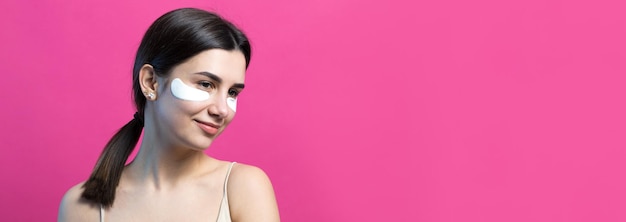 Close up portrait of pretty attractive girl with naked shoulders using patches under eyes Standing over pink background