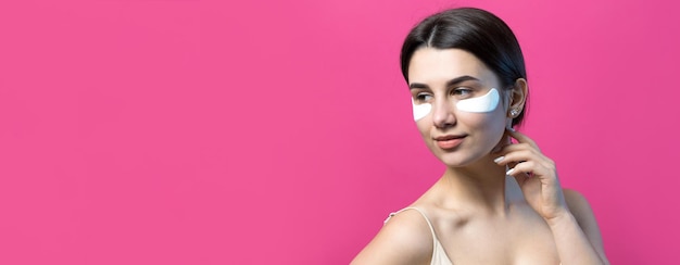 Close up portrait of pretty attractive girl with naked shoulders using patches under eyes Standing over pink background