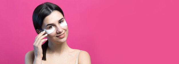 Close up portrait of pretty attractive girl with naked shoulders using patches under eyes Standing over pink background