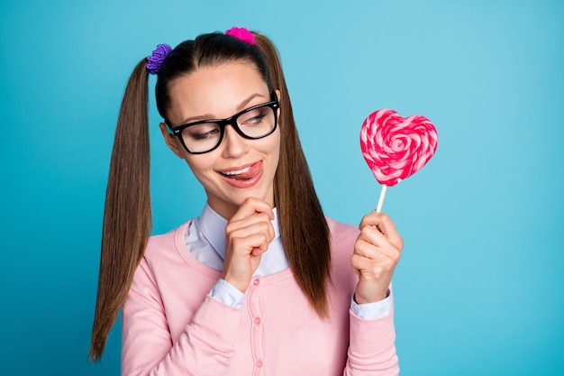 close-up portrait of pretty girlish cheerful college girl holding in hand candy licking lip