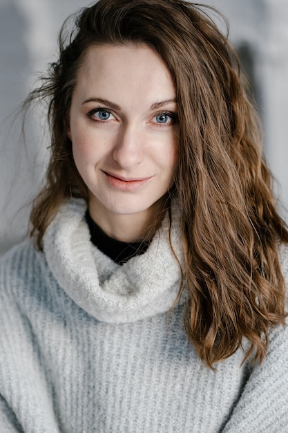 Close-up portrait of a pretty smiling young woman in cozy sweater looking directly