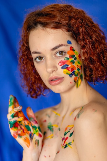 Close-up portrait of red curly haired woman Young cheerful soiled in paint. Portrait of a girl with a creative pattern on her face. Concept photography for art or women's blog