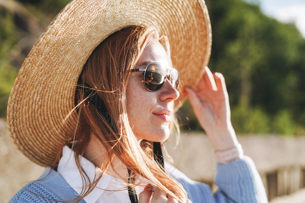 Primo piano ritratto di giovane donna dai capelli rossi in cappello di paglia sul paesaggio al tramonto