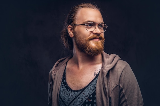 Close-up portrait of a redhead hipster male dressed in casual clothes standing in a studio, looking away. Isolated on the dark background.