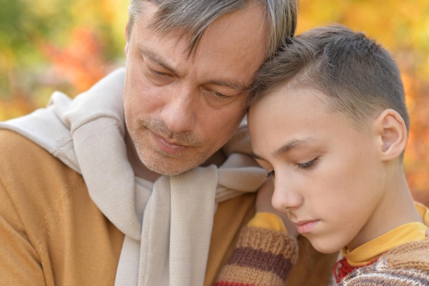 Close up portrait of sad father and boy in autumn park