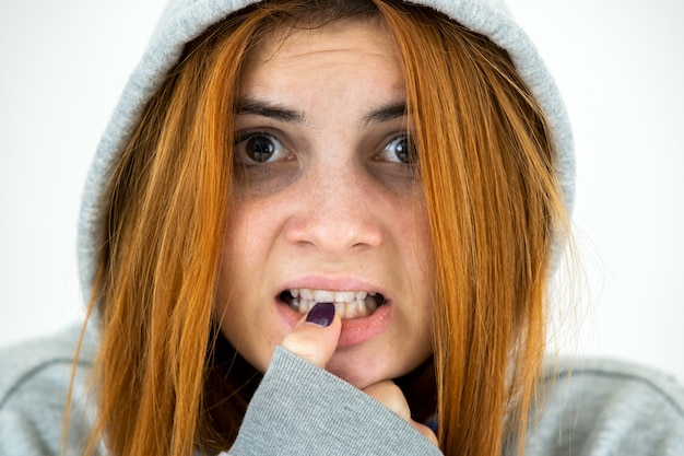 Foto chiuda sul ritratto di giovane donna spaventata di redhead che porta il pullover caldo di maglia con cappuccio.