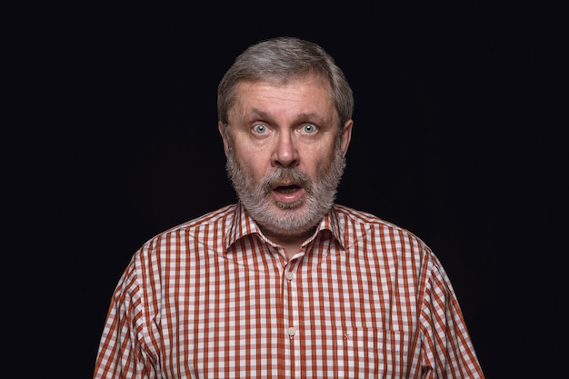 Close up portrait of senior man isolated on black studio wall