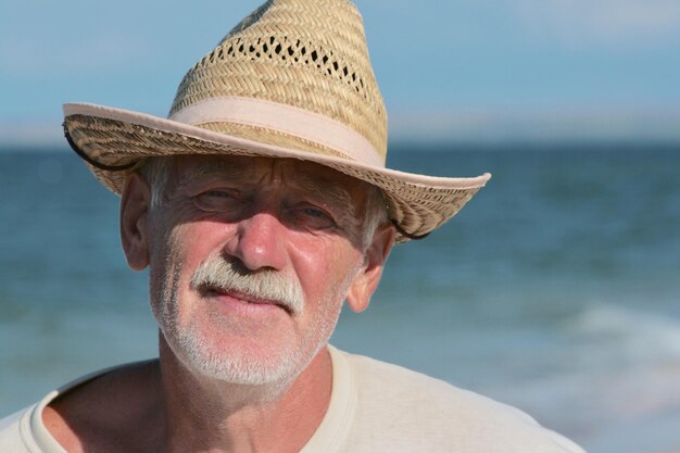 Close-up portrait of senior man standing at beach against sky during sunny day