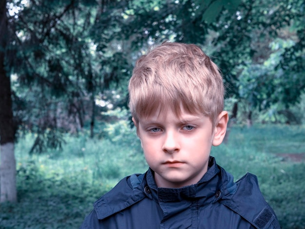 close-up portrait of serious boy wearing raincoat in forest