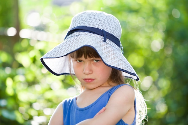 Close-up portrait of serious little girl in a big hat. Child having fun time outdoors in summer.