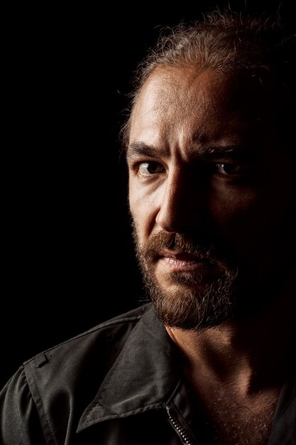 Close up portrait of a serious pensive middle-aged bearded man in dark