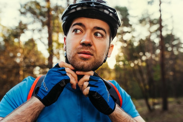 Close up portrait of serious and thoughtful cyclist close the protective helmet outdoors and looking away thinking about the route Travel concept Sport lifestyle Young rider wearing blue tshirt