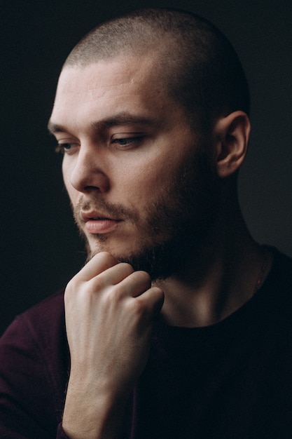 Close-up portrait of a serious young man looking away on a gray space. bald with a beard